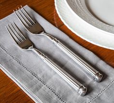 two silver forks sitting on top of a table next to a white plate and napkin