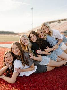 a group of young women sitting on top of a red carpet in front of an empty bleachers