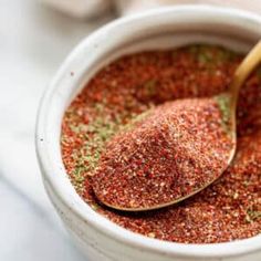 a white bowl filled with spices and a wooden spoon full of seasoning next to it