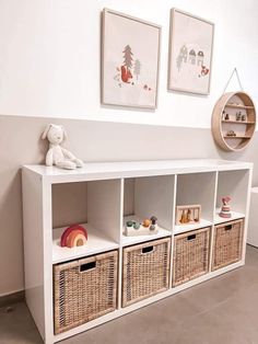 a white shelf with baskets and pictures on the wall next to a stuffed animal toy