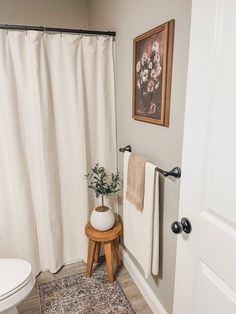 a white toilet sitting next to a wooden stool near a shower curtain in a bathroom