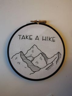 a white wall hanging with a black and white embroidery on it that says, take a hike