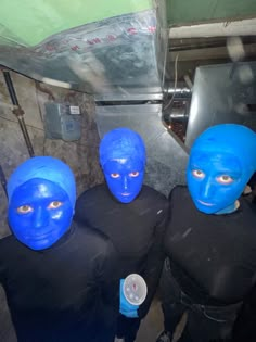 three people wearing blue paint on their face and body in front of a metal object