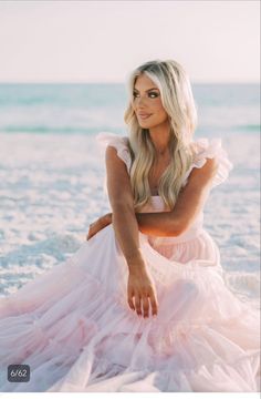 a woman in a pink dress sitting on the beach