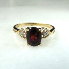 This is a beautiful, vintage 14K yellow gold garnet & diamond gemstone ring.  The oval garnet is 5.9mm x 7.8mm which is roughly .98 carat.  There are 2 round 1.5mm diamonds set on either side of the garnet.  The diamonds have overall H color with SI1 clarity.  Their total carat weight is 0.03ct.  The band is sized at 7 3/4.  Total weight of the ring is 2.3 grams.  The inside of the band is stamped FTJ 10K LIND.   This is a vintage, previously owned ring.  Therefore, light wear can be expected. Garnet And Diamond Ring, Garnet Gem, Red Band, Multi Stone Ring, Multi Stone, Diamond Gemstone, Gemstone Ring, Stone Rings, Beautiful Rings