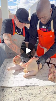 two men in aprons are cutting chicken on a table