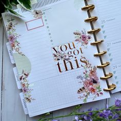 an open planner book sitting on top of a table next to purple flowers and greenery