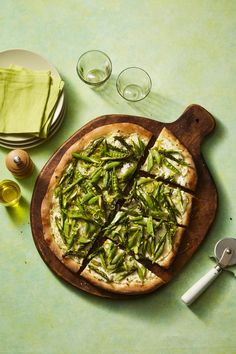 a pizza sitting on top of a wooden cutting board next to glasses and utensils