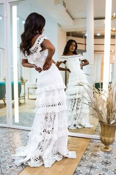 a woman standing in front of a mirror wearing a white dress with tiered ruffles