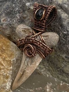 a wire wrapped brooch sitting on top of a rock next to a stone wall