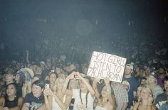 a group of people sitting in front of a crowd at a concert holding up signs