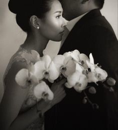 a man and woman standing next to each other with orchids in their hands, black and white photo