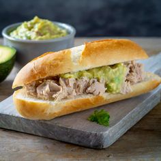 a sandwich with meat and guacamole on a cutting board next to an avocado