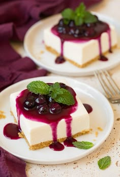 two white plates topped with cheesecake covered in blueberry sauce