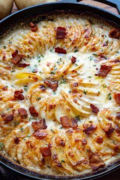 a baked dish with potatoes and bacon in a skillet on a wooden table top