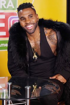 a man sitting at a table in front of a yellow sign and wearing a fur coat