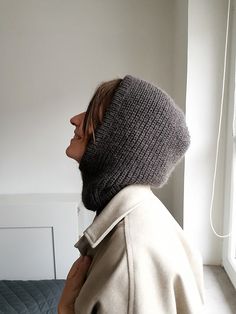 a woman wearing a knitted hat and coat looks out the window in her bedroom