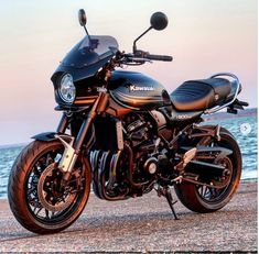 a black motorcycle parked on top of a sandy beach next to the ocean at sunset