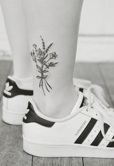 a woman's foot with a flower tattoo on her left ankle and white adidas sneakers