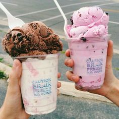 two people holding up ice creams in front of the camera, and one has an empty cup