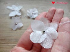 a hand holding some white flowers on top of a wooden table next to beads and thread