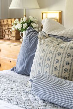 a bed with blue and white pillows on top of it next to a dresser filled with flowers