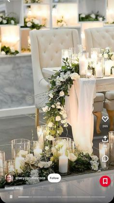 a table with candles, flowers and greenery in front of a white chair set up for a wedding reception