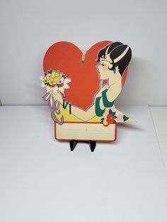 a heart shaped card with a woman holding a flower in her hand on top of a wooden stand