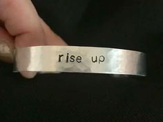 a hand holding a silver bracelet that says rise up