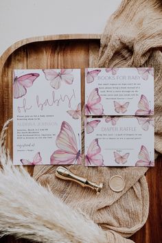 the wedding stationery is laid out on a wooden tray with feathers and butterflies around it