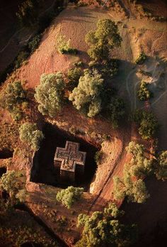 an aerial view of a building in the middle of some trees and dirt area with no people around it