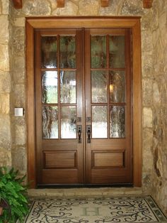 two wooden doors with glass on the side of a stone wall next to a potted plant