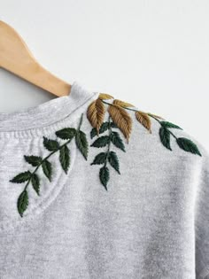 a white sweater with green leaves on it and a wooden hanger in the background