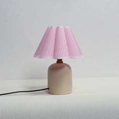 a pink and white table lamp with a light shade on the top, sitting on a white surface