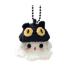 a black and white hat with yellow eyes hanging from a chain on a white background