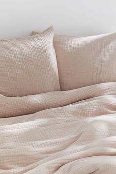 an unmade bed with beige sheets and pillows on top of it, next to a white wall