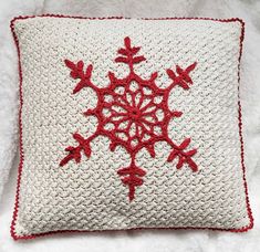 a crocheted snowflake pillow on a white blanket with red trimmings