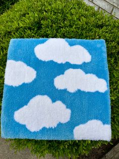 a blue rug with white clouds on it in the middle of some green bushes and shrubbery