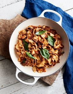 a pan filled with pasta and spinach on top of a wooden cutting board next to a blue towel