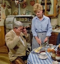 an old man and woman sitting at a table with food in front of them on the phone