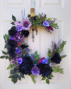 a wreath with purple flowers and greenery hanging on a door