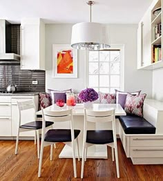 a kitchen with white walls and wooden flooring next to a dining room table filled with chairs