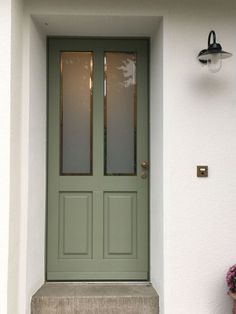 a green door with two sidelights and potted plants on the steps outside it