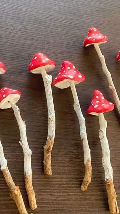 small red mushrooms are lined up on the wooden table, with sticks sticking out of them