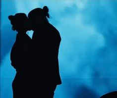 the silhouette of two people kissing in front of a blue background