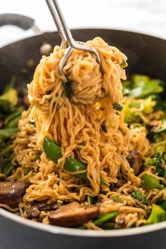 noodles and vegetables being cooked in a wok with tongs, close up view