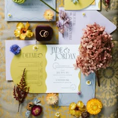 the wedding stationery is laid out on top of yellow and blue paper with flowers