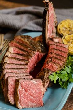 the steak is cut into pieces on the blue plate with parsley and lemon wedges