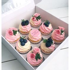 a box filled with cupcakes covered in pink frosting and topped with blueberries