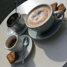 there is a cup of coffee on the table next to two cookies and spoons